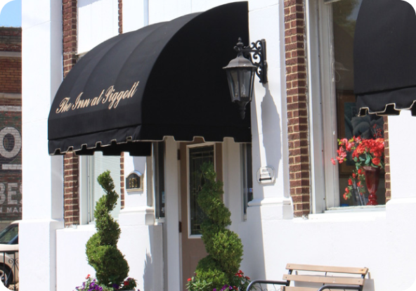 The image shows the entrance of a building with a black awning that reads "The Inn at Sligo." The doorway is flanked by two spiral-shaped topiary plants and a vintage-style black lamp.